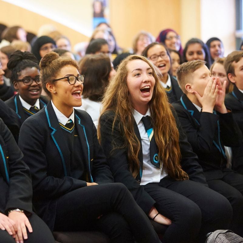 A group of secondary school children laugh at a performance