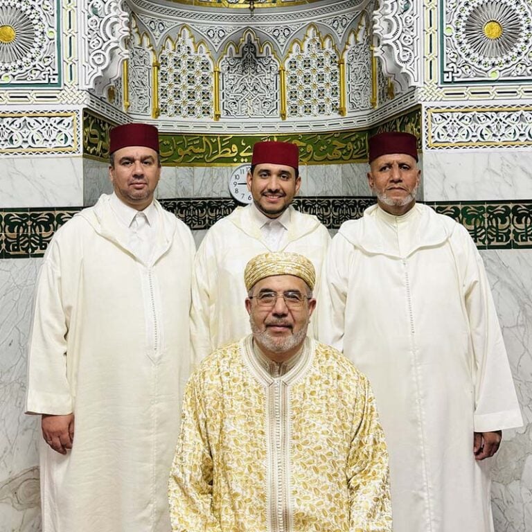 The Fez Singers stood together in white outfits in a beautifully ornate hall.